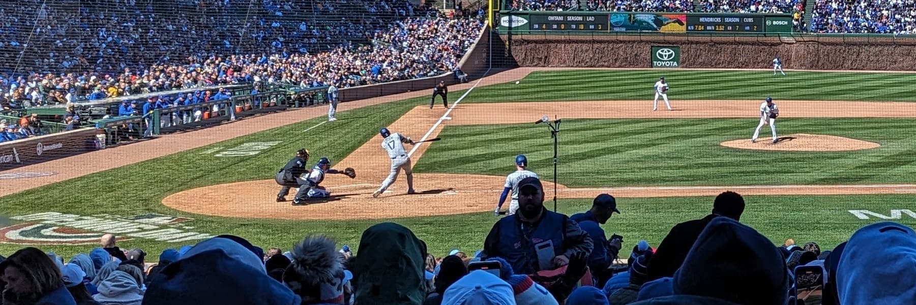 A wide in-game view from the stands at a Cubs game, capturing the action at the plate and a packed ballpark.